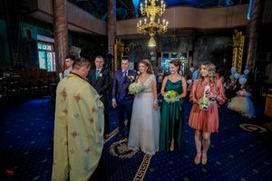 Wedding party guests in formal attire gather at an elegant venue with ornate chandeliers.