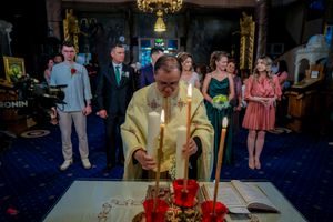 A priest in ceremonial gold vestments conducts a religious service at an altar with lit candles.