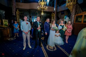 A wedding ceremony takes place in a traditional church with blue carpet and ornate gold decorations.