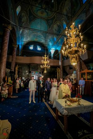 Ornate church interior with golden chandeliers and blue ceiling during a wedding ceremony.