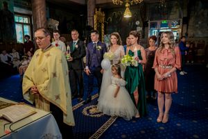Wedding party and clergy gather in formal attire during an ornate church ceremony.