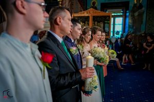 Wedding party stands in line during ceremony on blue carpet with decorative church interior visible.