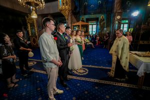 Orthodox wedding ceremony in progress with priest in gold robes leading service on blue carpeted floor.