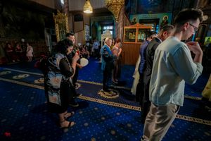 Photographers capture moments during Orthodox church wedding ceremony on blue carpeted floor.