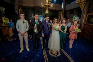 Wedding party poses for formal photo on blue carpet in decorated church with ornate gold details.