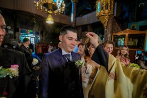 Priest performs blessing ritual during Orthodox wedding ceremony in ornate church interior.