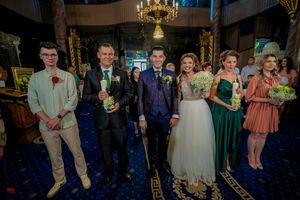 Wedding party members line up in formal attire inside ornate church with blue carpeting.