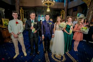 Wedding group poses on decorative blue carpet under elegant chandelier in church setting.