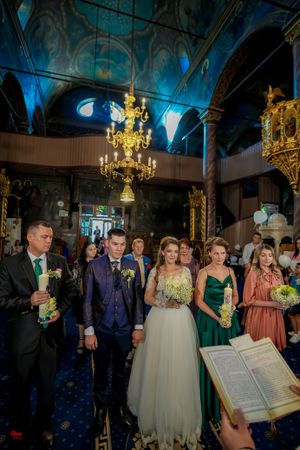 Wedding ceremony in a grand hall with blue lighting and ornate gold chandeliers.