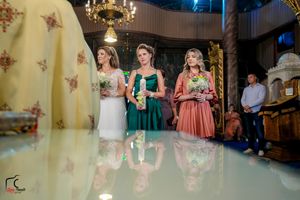 Three attendants in formal attire hold decorated candles during an elegant church ceremony.