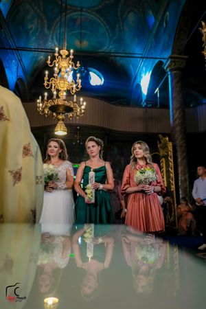 Wedding party members in formal attire standing beneath ornate gold chandelier.