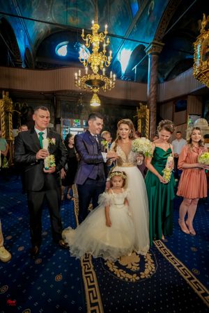Wedding party gathered under ornate chandelier in church with blue-lit vaulted ceiling.