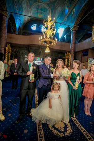 Orthodox wedding ceremony in ornate church with blue lighting and elegant chandelier overhead.
