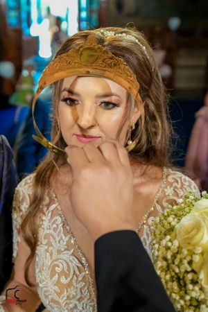 Bride wearing lace dress and golden crown makes playful expression during ceremony.