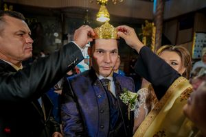 Orthodox wedding ceremony participants adjust ceremonial crown in church interior.