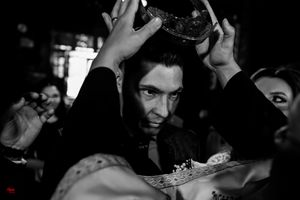 Dramatic black and white photo of Orthodox wedding crown ceremony in dim lighting.