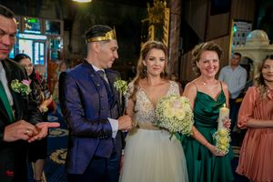 Wedding ceremony in traditional Orthodox church with bride in white dress and groom in navy suit.