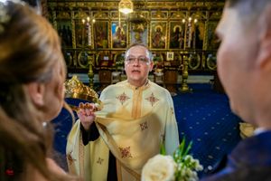 Orthodox priest performs traditional wedding ceremony in ornate church with golden iconostasis and blue carpet.