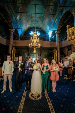 Wedding party poses in formal attire against blue-lit interior of ornate reception venue.