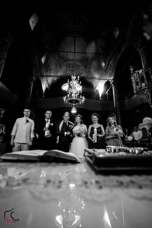 Black and white photo of wedding party standing behind candlelit table in ornate reception hall.