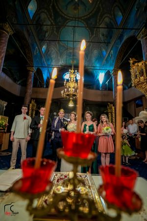 Wedding party stands in an elegant venue with blue lighting and chandeliers while red candles glow in the foreground.