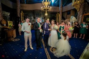 Wedding party gathered in ornate venue with blue carpet and chandeliers.