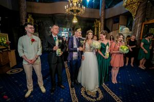 Wedding party gathers in ornate venue with blue carpet and chandelier lighting.