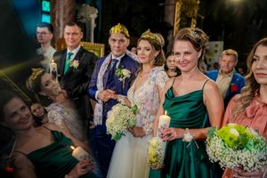 Wedding party poses together holding white floral bouquets with bridesmaids in emerald green dresses.