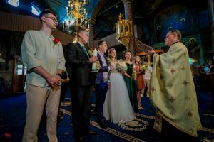Wedding party stands together in a grand hall with ornate chandeliers and decorative lighting.