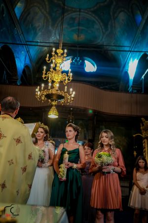 Wedding ceremony participants in formal attire beneath elegant church chandeliers and blue lighting.