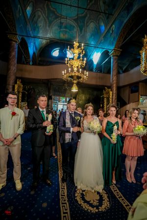 Wedding party gathered in ornate church interior with chandelier lighting and decorative ceiling.