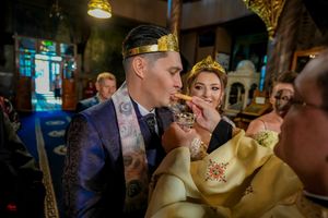 Orthodox wedding ceremony in a dimly lit church with ornate chandeliers and traditional religious attire.