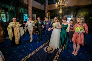 Orthodox church ceremony with guests standing on blue carpeted floor under chandeliers.
