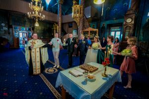 Wedding celebration in a dimly lit Orthodox church with traditional iconography and blue carpeting.