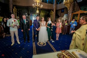 Wedding guests mingle in an ornately decorated reception hall with blue lighting and chandeliers.