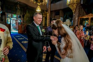 Wedding reception scene with guests gathered around decorated tables in a grand hall.