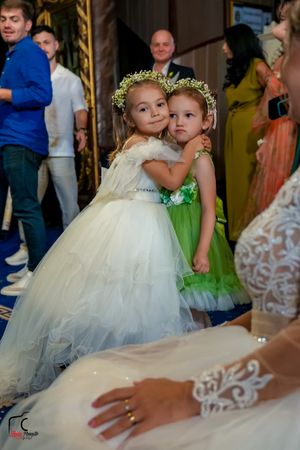 Two young flower girls in tulle dresses and floral crowns pose together at an elegant wedding reception.