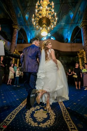 A couple dances at their wedding reception under an ornate chandelier in a grand ballroom with blue lighting.