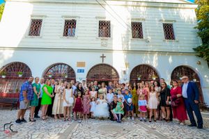 Large group of wedding guests gathered outside white church building for formal photos.