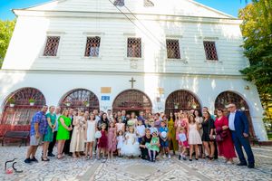Large group of wedding guests gathered outside white church building for formal photos.