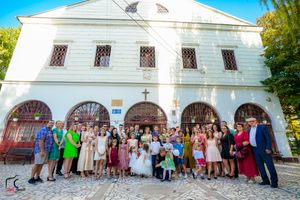 Large group of wedding guests gathered outside white church building for formal photos.