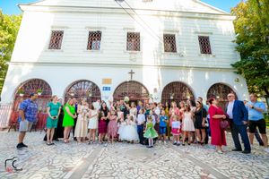 Large group of wedding guests gathered outside white church building for formal photos.