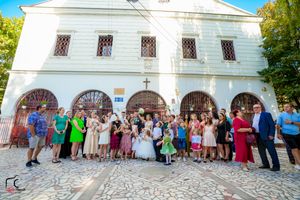 Large group of wedding guests gathered outside white church building for formal photos.