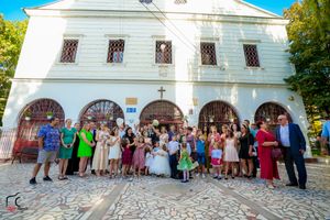 Large group of wedding guests gathered outside white church building for formal photos.