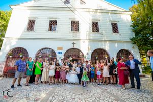 Large group of wedding guests gathered outside white church building for formal photos.