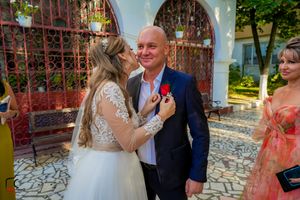 Wedding party members pose for formal photos against blue walls and red iron gates.