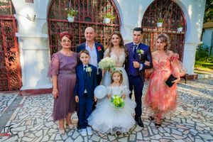Wedding party poses together on stone pavement in front of decorative red gates and white walls.
