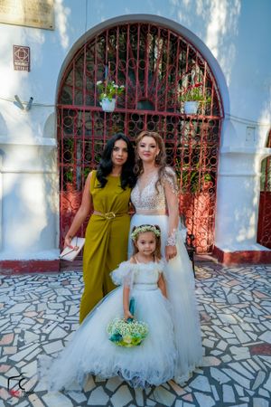 Wedding party members in white and yellow dresses pose against a blue wall with red iron gates.