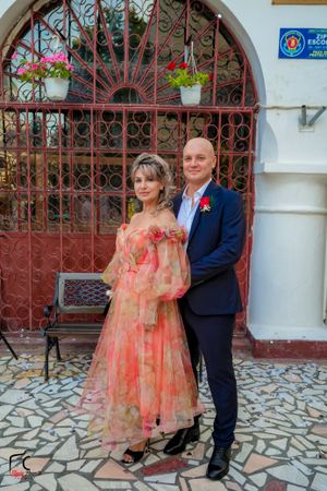 A couple in formal attire poses for photos in front of a church entrance with decorative gates.