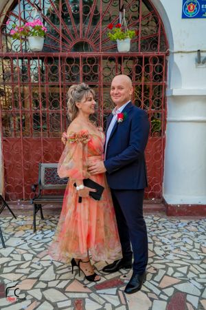 A couple shares a romantic moment in front of ornate red gates and white walls.